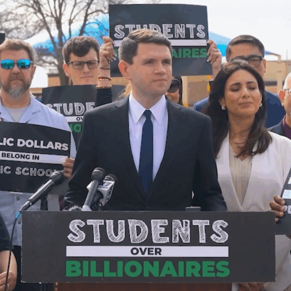 James Talarico speaks at a podium in front of Students Over Billionaires placard